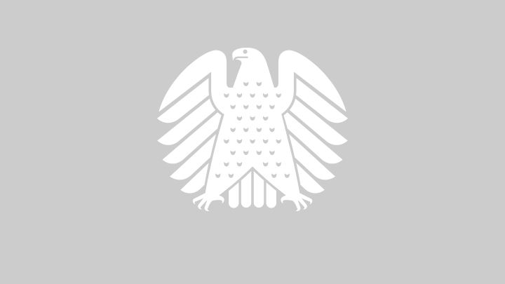Ein digitales Gedenkbuch erinnert an die verstorbenen Abgeordneten des Bundestages. Schwarz-weiß-Aufnahme der leeren Sitzreichen im Plenarsaal des Bundestages mit einem Trauergesteck auf einem Platz